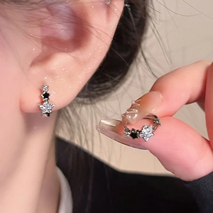Detalle de pendientes de estrella plateados con esmalte negro y circón blanco en modelo