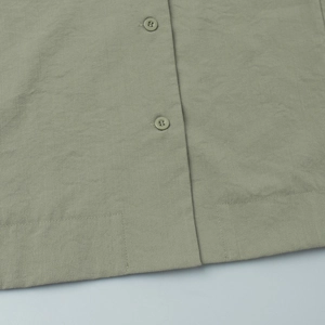 Detail of sage green linen shirt hem showing natural fabric texture and matching buttons