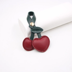 Detail of red cherry leather bag charm with green leaves and gold metal snap button
