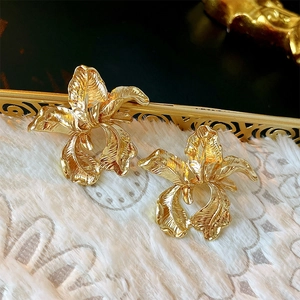 Golden irregular flower earrings with metallic brushed texture on white plush background