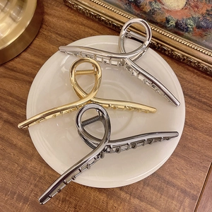 Three oversized metal shark hair claws in silver, gold, and grey on a white plate