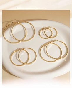 Set of four pairs of polished gold hoop earrings in various sizes on a white ceramic tray