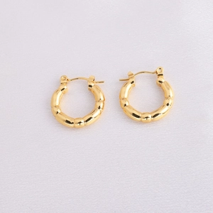 Detailed close-up of golden bamboo-style hoop earrings on light pink textured fabric