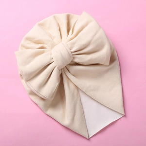 Detailed view of a soft cream baby turban hat with a large decorative bow