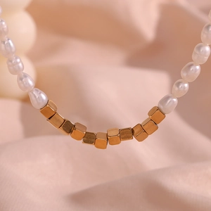 Macro shot of freshwater pearls and matte gold square beads on a beaded necklace