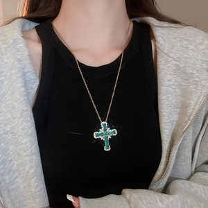 Gros plan d'un collier croix doré avec pierre vert émeraude et cristaux scintillants