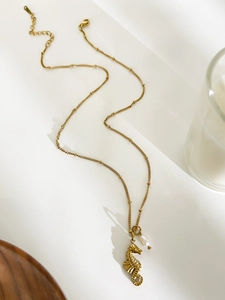 Close-up of golden seahorse pendant necklace with pearl on elegant wooden surface