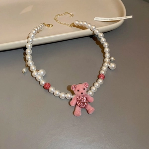Macro view of white faux pearl necklace featuring a pink flocked bear charm with rhinestone