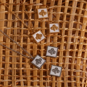 Detail of gold and silver bee square pendant necklaces and earrings on a woven mat
