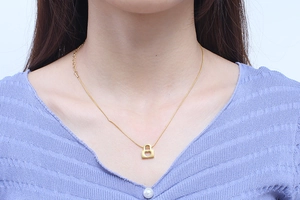 Close-up of a gold heart locket pendant on a sleek snake chain worn by a model