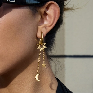 Boucles d'oreilles pendantes étoile et lune dorées portées sous une lumière naturelle