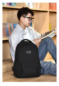 Detail view of a black canvas backpack next to a person reading in a library setting