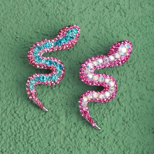 Detail view of colorful rhinestone snake-shaped earrings on a green textured surface