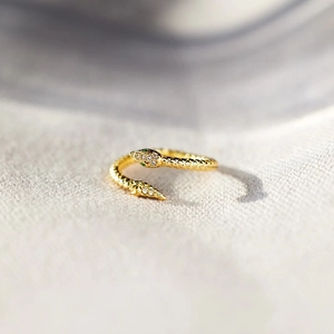 Macro detail of gold snake ring featuring green gem eyes and sparkling white crystals
