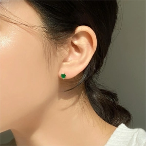 Macro shot of a heart-shaped green zircon earring in a claw setting worn by a model