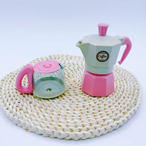 Close-up of pink and green toy moka pot and transparent coffee pot on a woven mat