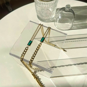 Detail of 18K gold emerald pendant with Cuban and fine link chain on glass display