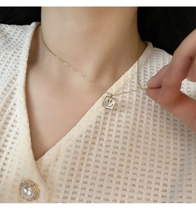 Close-up of gold-plated square shell necklace featuring a smiling face pendant on a model