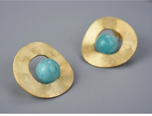 Macro detail of matte gold geometric stud earrings with polished green stone beads