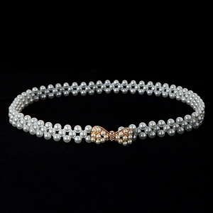 Detail view of a white pearl beaded belt with an elegant gold bow-shaped buckle