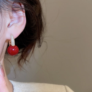 Detailed close-up of a red round bead earring with gold diamond-encrusted ear buckle