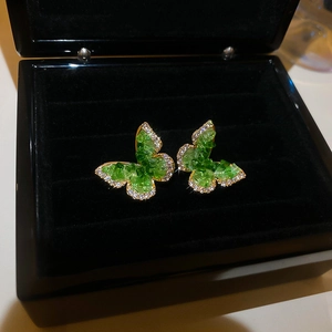 Detailed macro view of green butterfly earrings with glittering crystals and gold metal edges