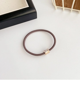 Detail of a brown elastic hair tie featuring a small gold metal piece with rhinestones