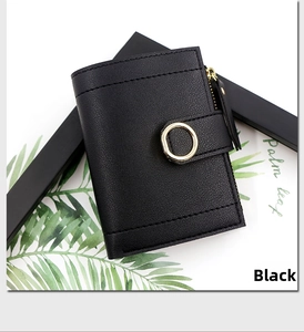 Detail of black pebbled leather wallet with gold ring buckle on palm leaf background