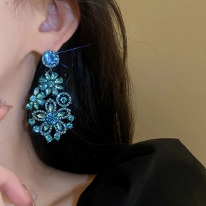 Close-up of vintage blue rhinestone flower drop earring worn by a model in soft light