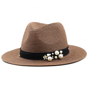 Close-up of brown woven sun hat featuring black elastic band with pearls and gold studs