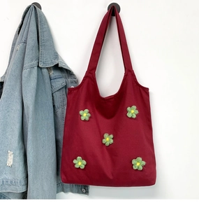 Detail of red canvas tote bag featuring 3D knitted green flowers and sturdy handle strap
