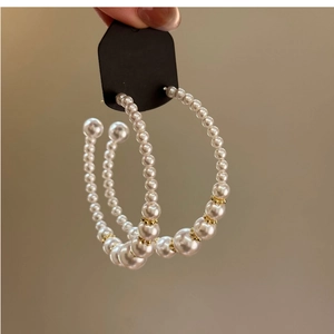Detailed view of hand holding gold C-shaped earrings with pearl and metallic bead clusters