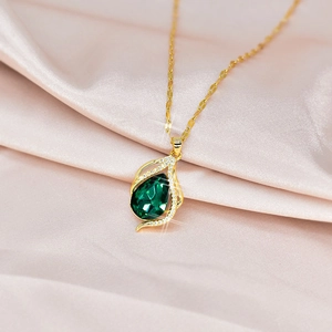 Gold teardrop necklace with green pear-shaped gemstone on soft pink silk fabric