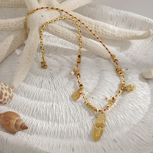 Detail of woven rope necklace with surf charms, pearls and gold beads on beach decor