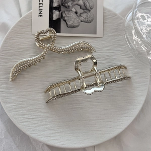Set di eleganti mollette per capelli dorate con perle bianche e strass su un piatto
