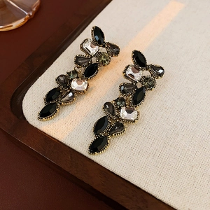 Détail de boucles d'oreilles dorées vintage avec cristaux noirs et clairs sur tissu