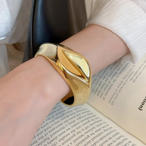 Detailed view of wide gold acrylic bangle with wavy texture on female wrist