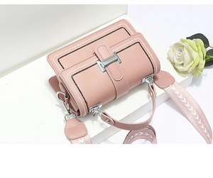 Pink crossbody bag with embroidered border and herringbone strap on a white stand