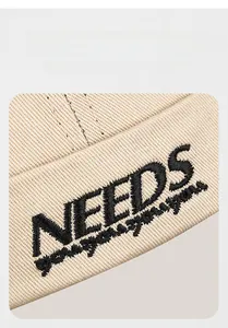 Vue détaillée du tissu sergé beige avec broderie 3D NEEDS noire sur le bonnet