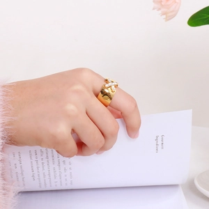 Detail of 18K gold-plated X-shape zircon wide ring on model's hand with elegant book