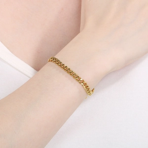 Close-up of a polished gold Cuban link chain bracelet worn on a female wrist