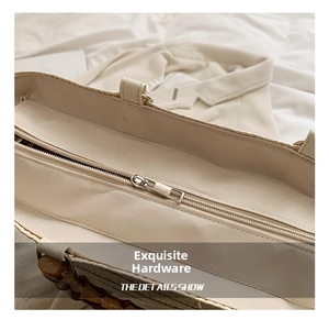 Detail shot of a beige straw tote bag with bamboo handle and smooth metal zipper