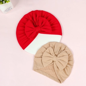 Close-up of red and beige newborn turbans with big bows on ribbed knit fabric