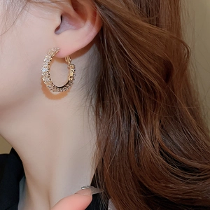 Close-up of golden hoop earrings with pavé-set zircons worn by a female model