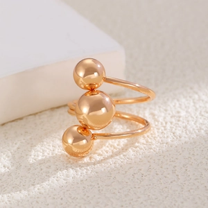 Macro detail of multilayer spiral metal ring with polished gold beads on stone background