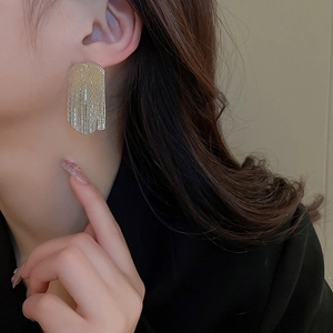 Close-up of gold irregular geometric fringe earrings with textured vertical patterns