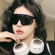 Close-up of black oversized shield sunglasses paired with white over-ear headphones