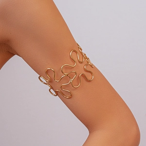 Detail of gold hollow wavy arm cuff showing polished metallic texture on upper arm