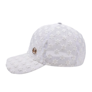 Détail d'une casquette en dentelle blanche avec broderies florales et logo M en métal