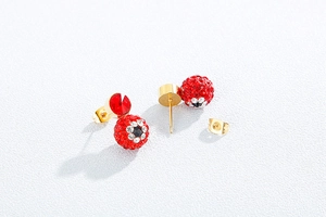 Detailed close-up of golden stud earrings featuring red crystals and eye-pattern motifs